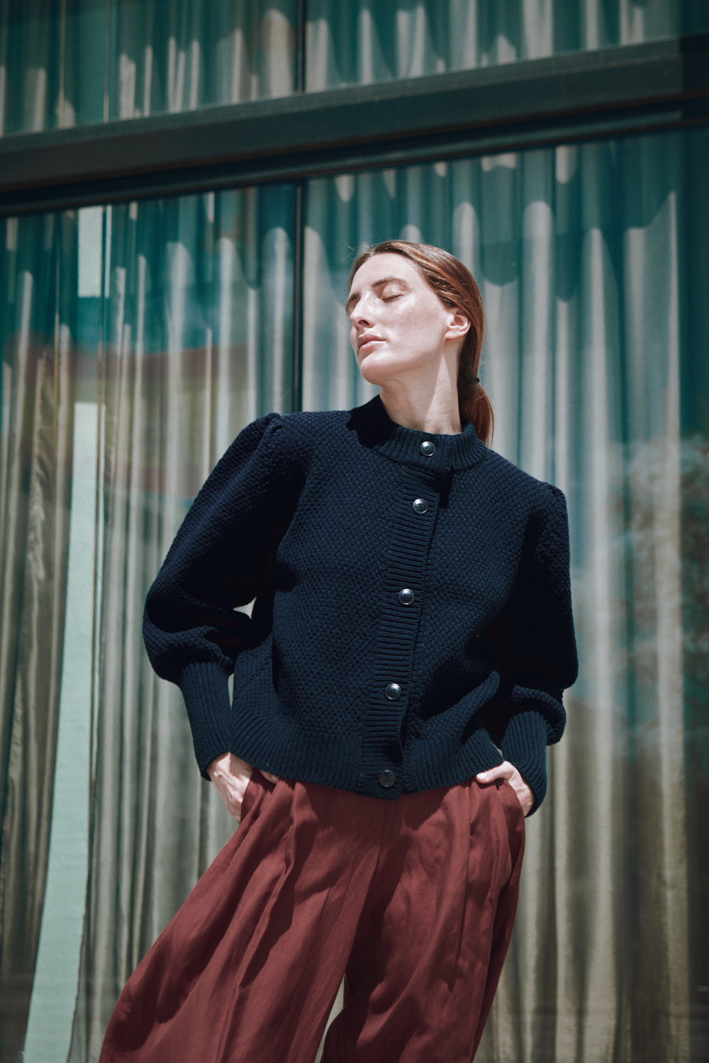 Woman wearing a dark blue L'ENVERS cardigan and red skirt standing in front of a glass building.
