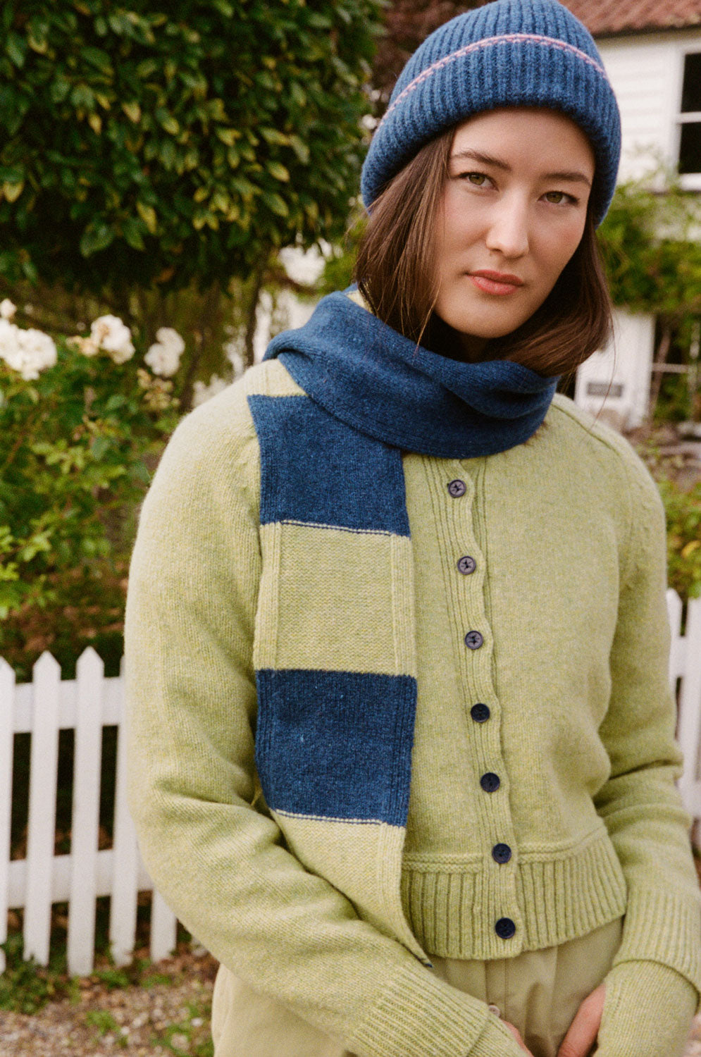 Model wearing an Atlantis blue ribbed beanie with pink trim, styled with a lime cardigan and blue and lime scarf.