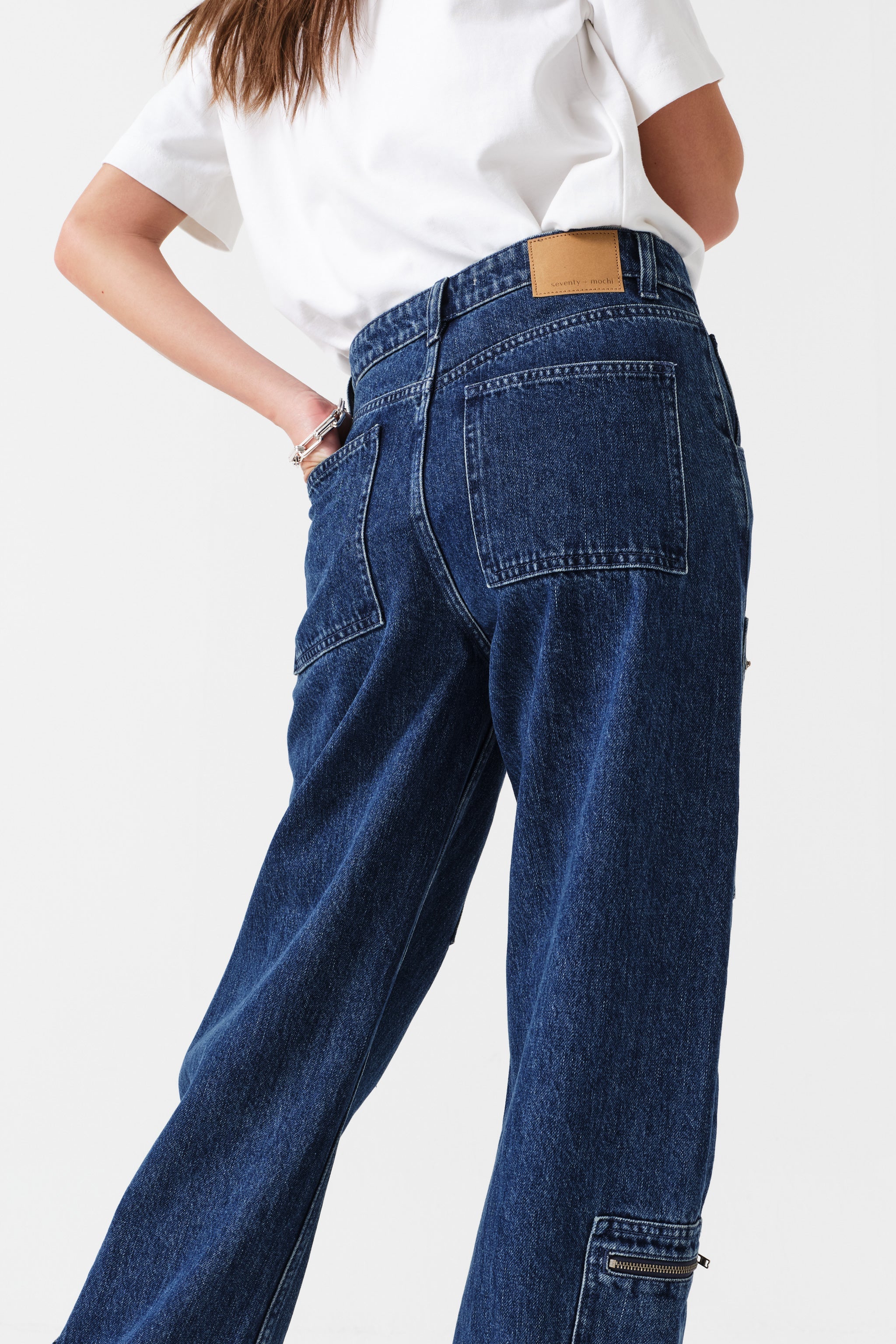 Woman wearing a white t-shirt and blue jeans with zip details on a white background