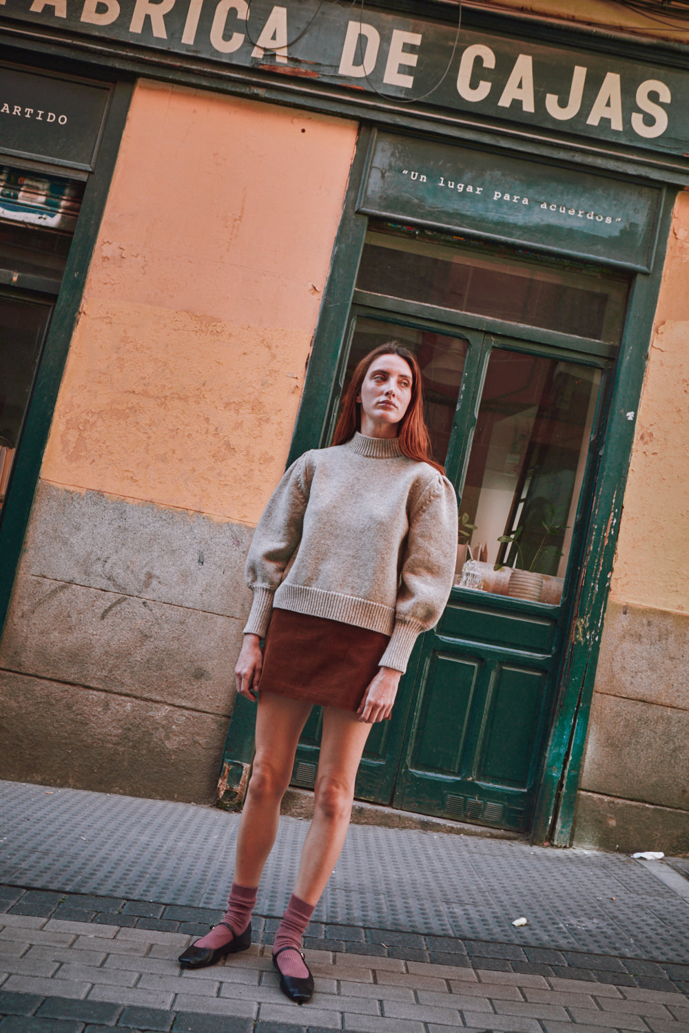 Woman wearing a beige L'ENVERS sweater standing in front of a building