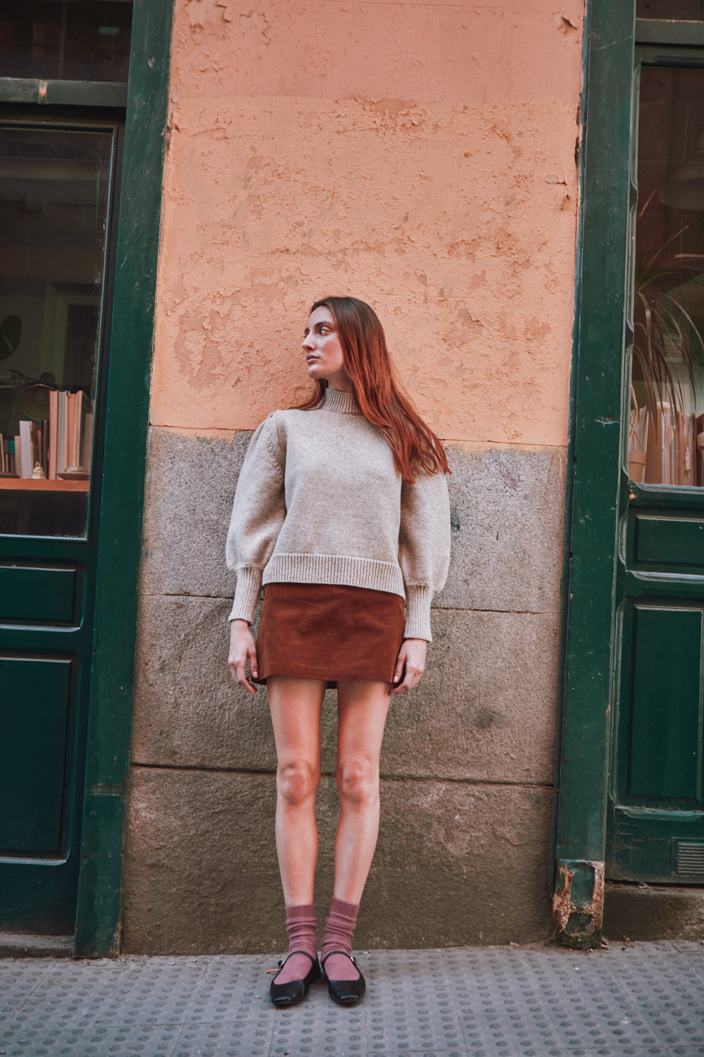 Woman wearing a beige L'ENVERS sweater standing in front of a building
