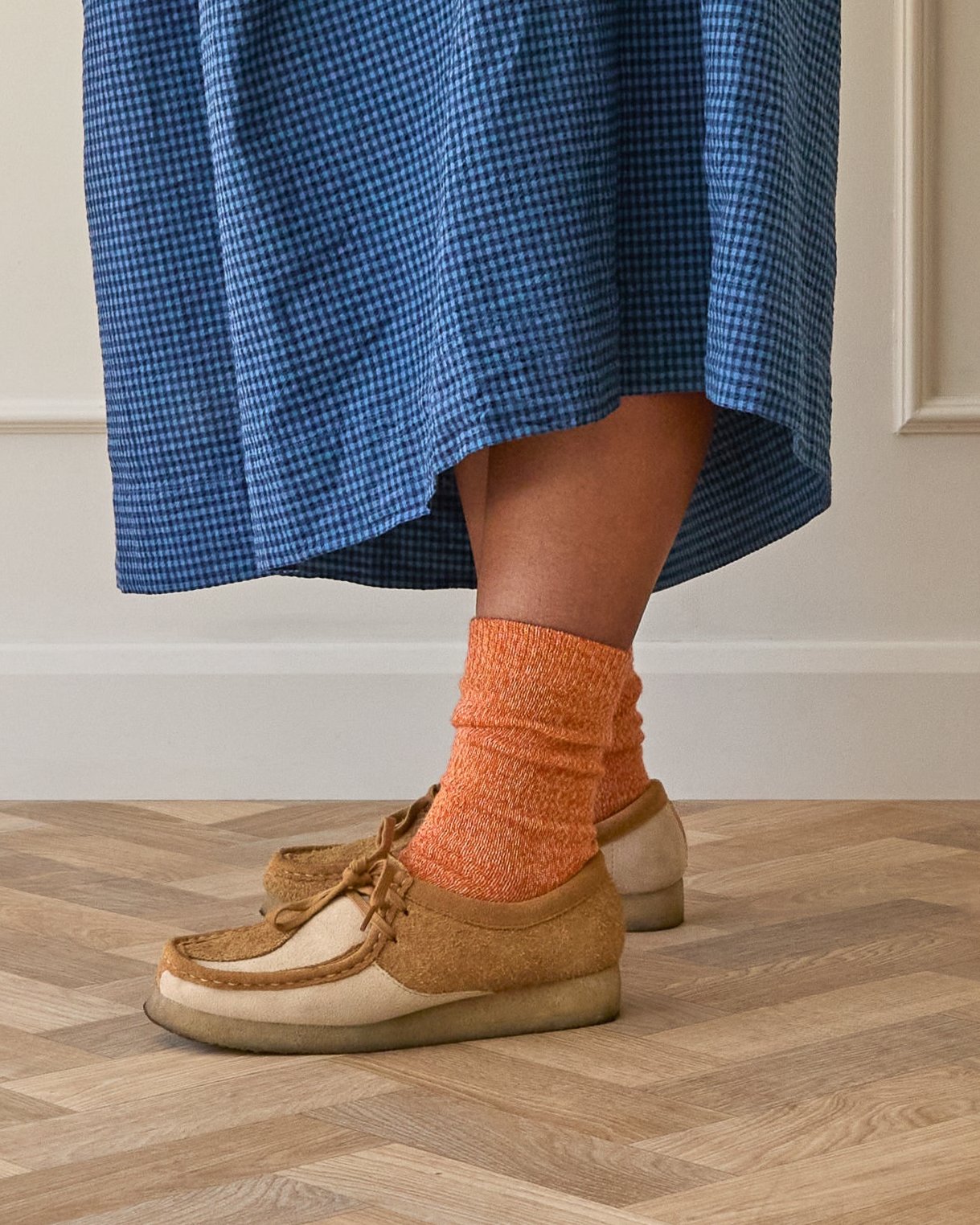 Model wears orange wool socks, knitted in soft merino wool. Designed and made in Britain.
