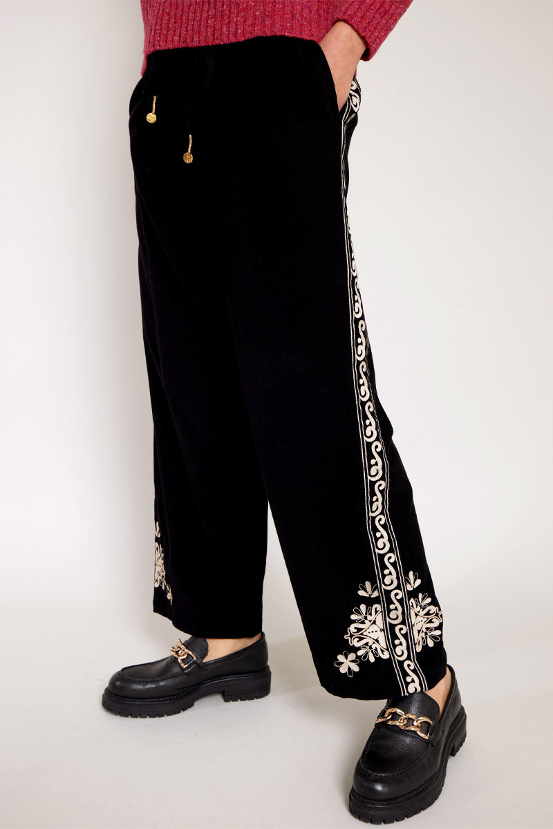side view of Models legs with hands in pockets wearing East Eveline embroidered trousers, with pink Oubas knitted jumper