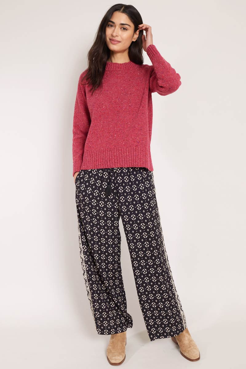 Model wearing East Kaia Trousers, with knitted jumper, tucking hair behind ear