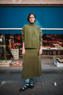 Person wearing a green outfit standing in front of a market stall 