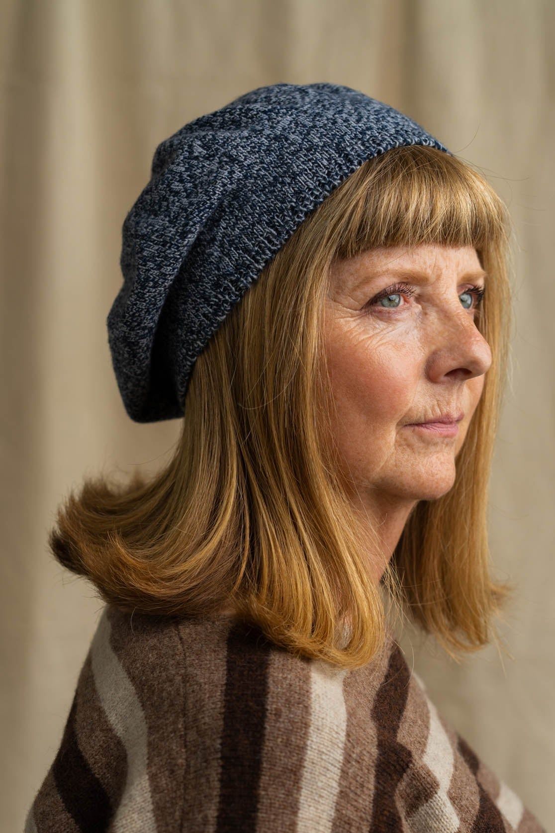 Woman wearing a blue knitted hat and striped jumper against a beige background
