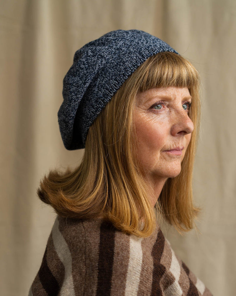 Woman wearing a blue knitted hat and striped jumper against a beige background