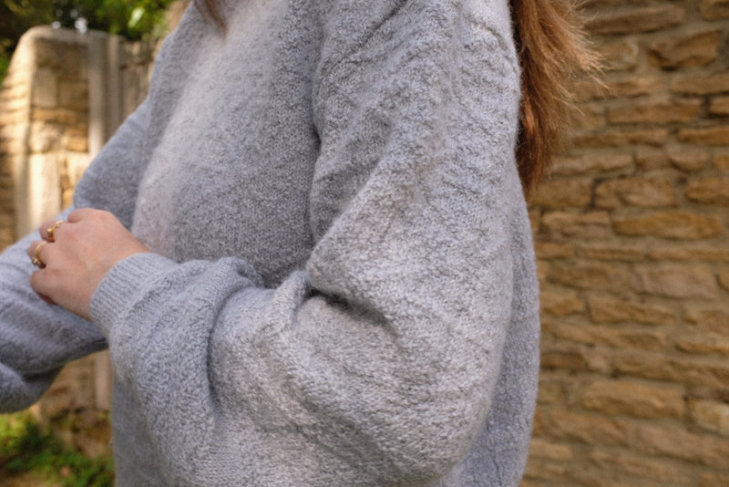 Light grey sustainable knitwear jumper with textured details, worn casually outdoors.