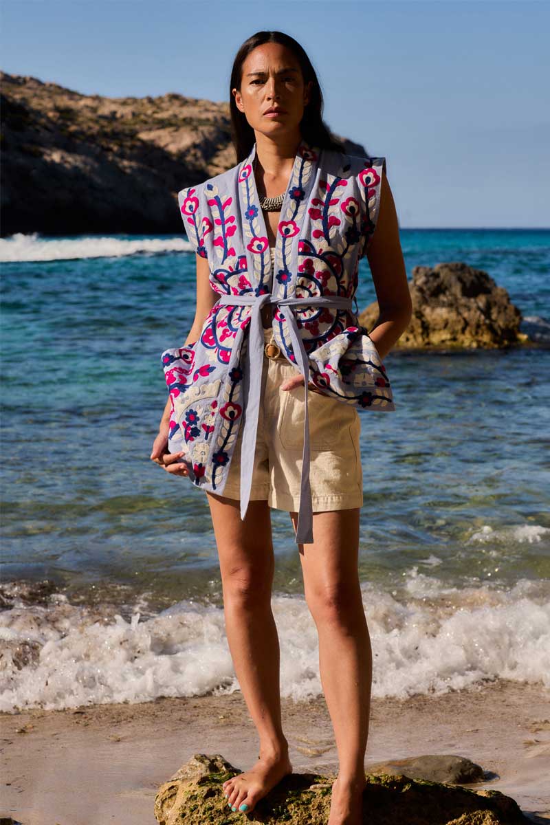 Model stands on a rock on the beach wearing East Dora Embroidered Gilet