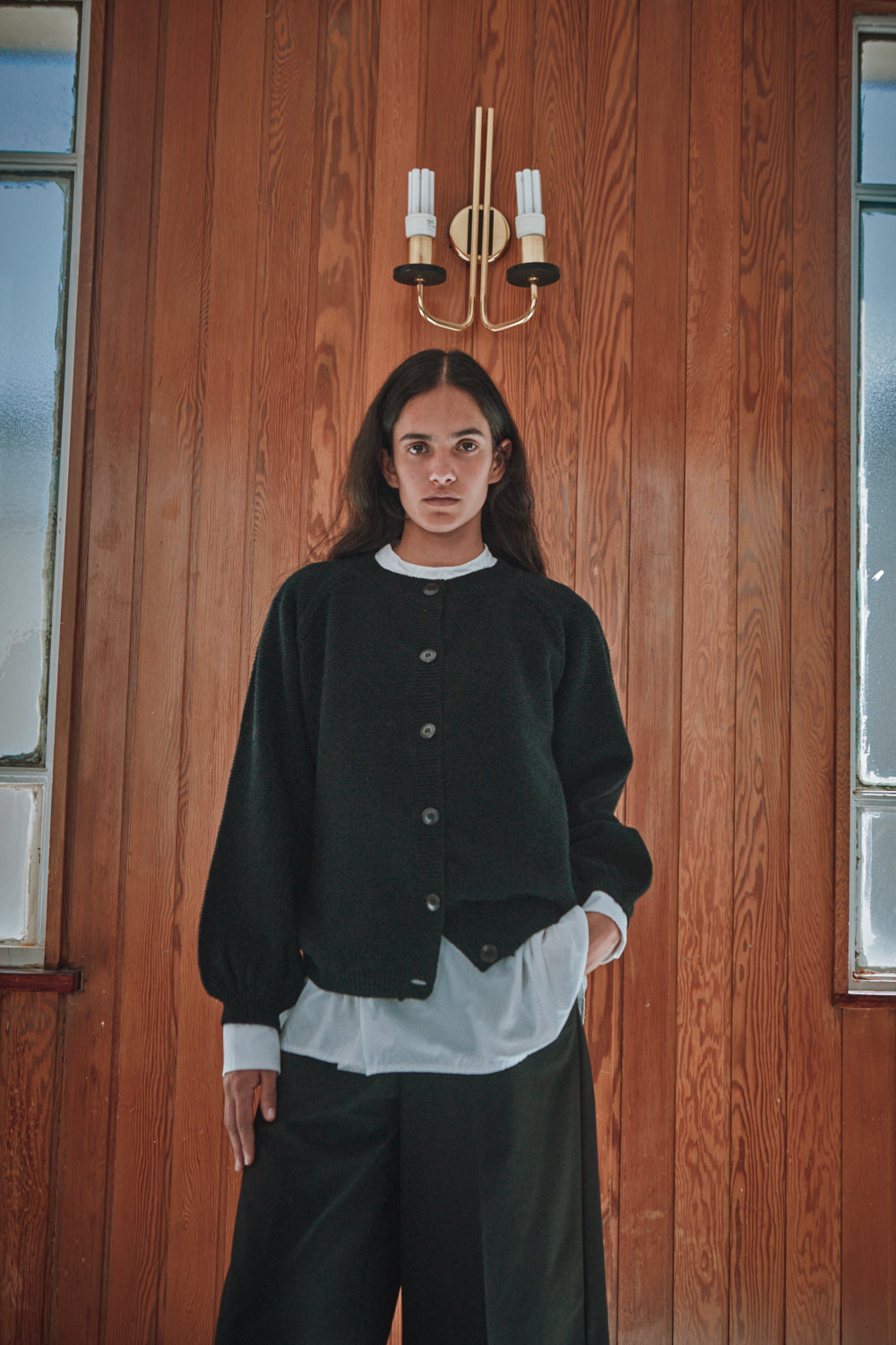 Person wearing a black jacket and white shirt against a wooden wall.