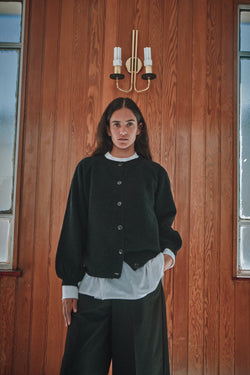 Person wearing a black jacket and white shirt against a wooden wall.
