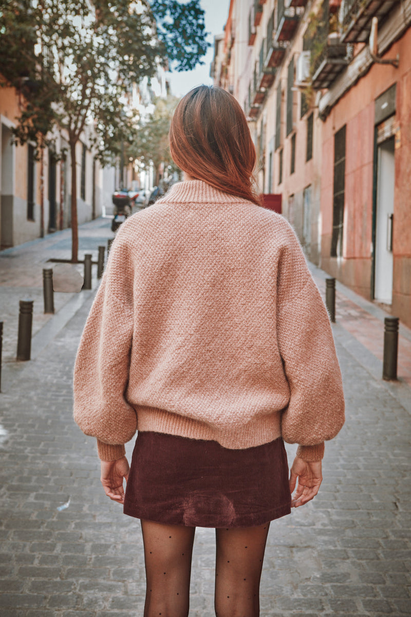 Person wearing a pink sweater and maroon skirt walking down a street.