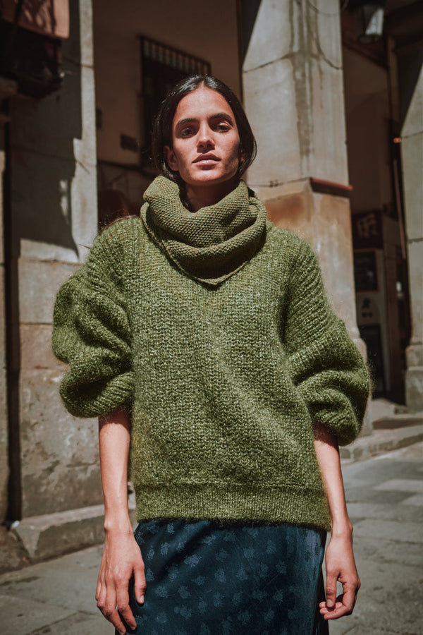 Person wearing a green knitted sweater standing on a street.