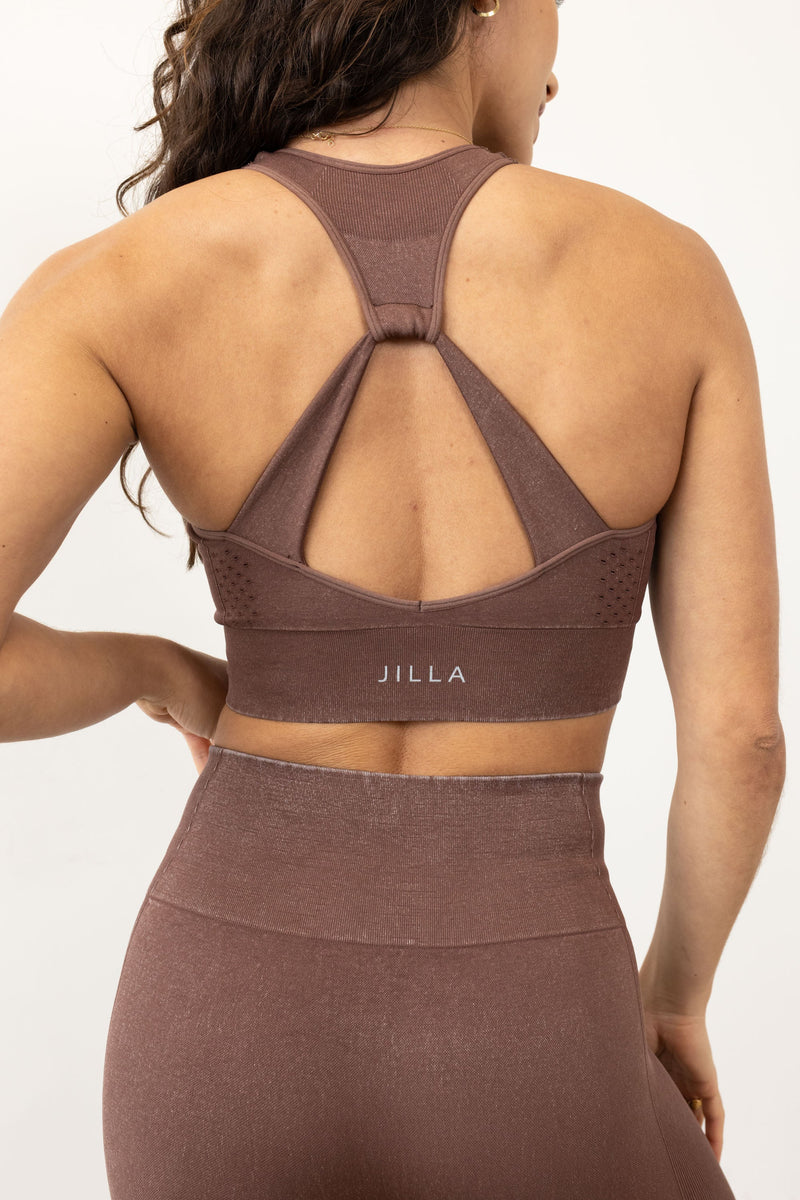 Meet our chocolate brown Aquarius Recycled Sports Bra - uniquely textured and stylish, perfect for yoga, barre, and more. Crafted from soft recycled seamless fabric, it offers light to medium support with a high neckline and statement back shape. Pair with our matching leggings for a seamless studio-to-street look. Enjoy versatile support and comfort, customizable with removable pads by sustainable activewear brand Jilla Active