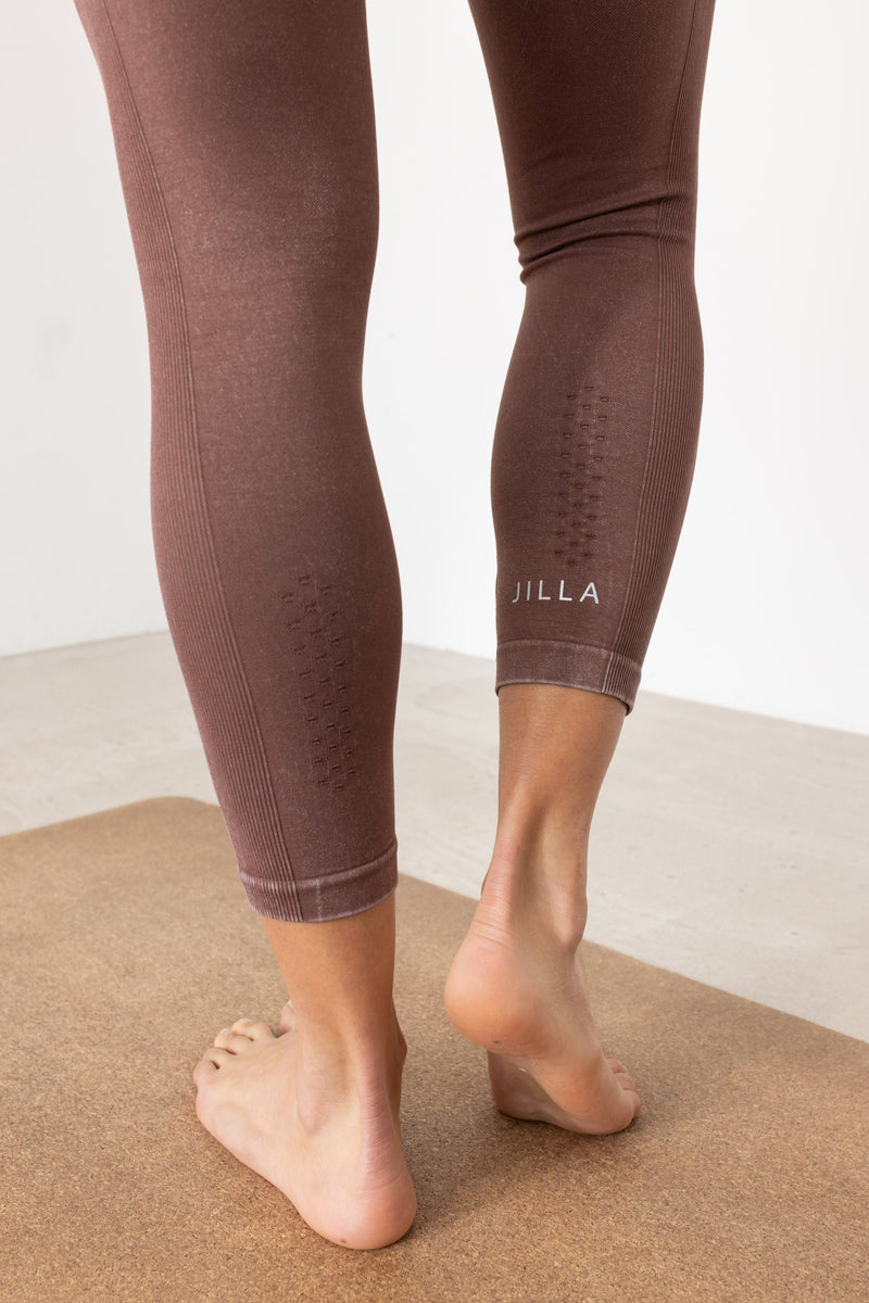 Our brown Aquarius Recycled Leggings - crafted for seamless performance in your yoga flows, barre workouts, and reformer classes. Made from four-way stretch fabric, they move effortlessly with you. Designed with flattering ribbing and an acid wash effect, each pair is unique. The high-rise ribbed waistband with internal elastic ensures they stay in place during your entire class, while the double-layered gusset provides all-day comfort and flexibility. Elevate your activewear game with Jilla Active