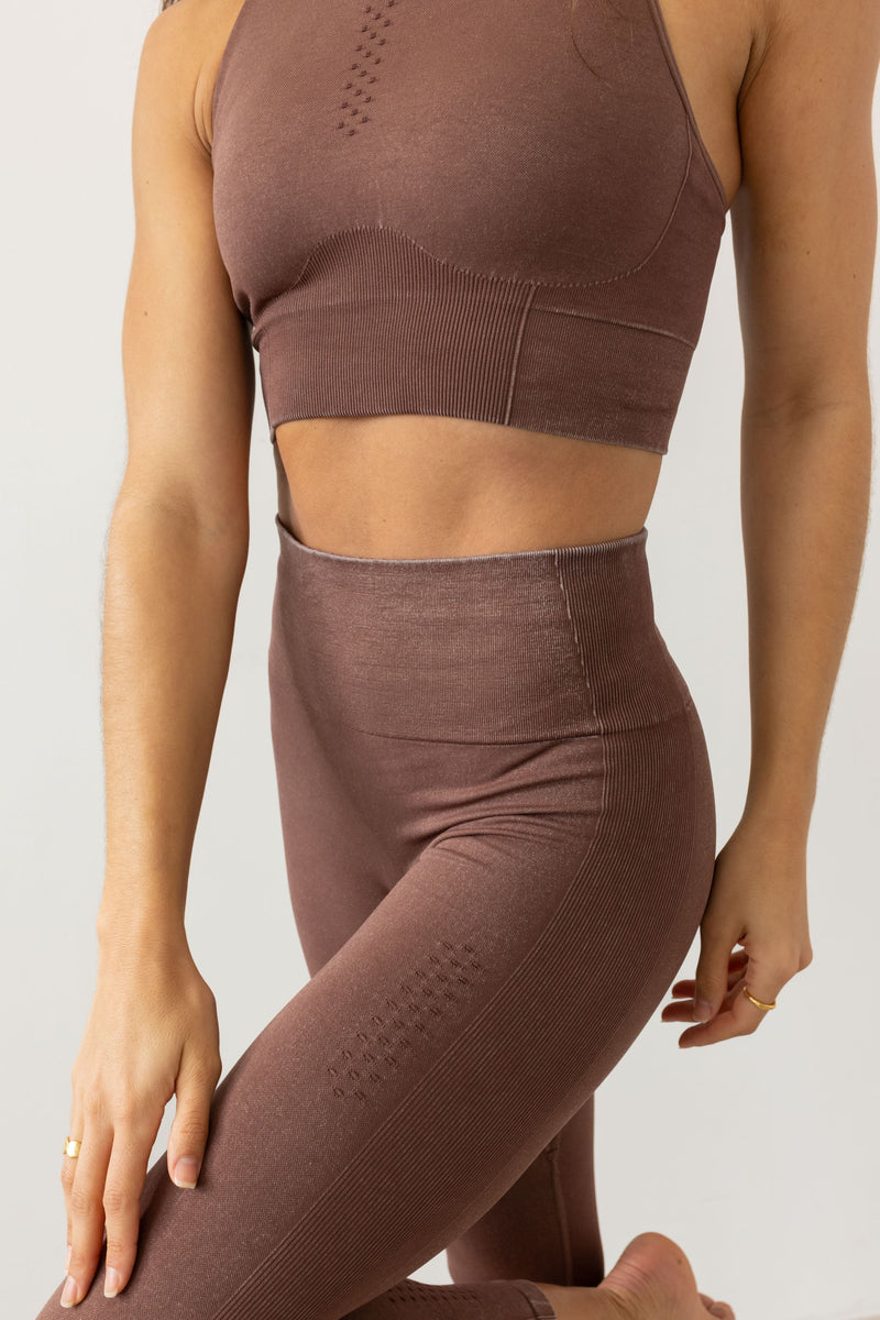 Meet our chocolate brown Aquarius Recycled Sports Bra - uniquely textured and stylish, perfect for yoga, barre, and more. Crafted from soft recycled seamless fabric, it offers light to medium support with a high neckline and statement back shape. Pair with our matching leggings for a seamless studio-to-street look. Enjoy versatile support and comfort, customizable with removable pads by sustainable activewear brand Jilla Active