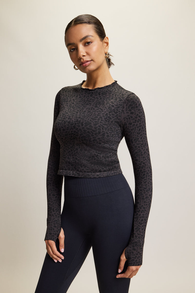 Black Sahara Recycled Long Sleeve Leopard Jacquard Top by Jilla Active – Seamless, stretchy activewear top made from recycled fabric, featuring thumbholes for added warmth, breathable material for comfort during workouts, and stylish neck detailing. Perfect for gym sessions, yoga, lounging, or casual wear, and part of a matching set with coordinating leggings and bra.