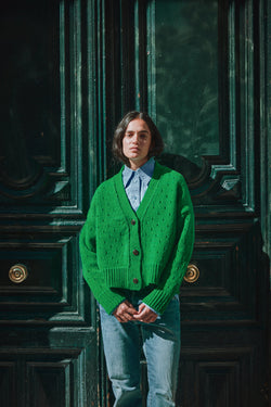 Person wearing a green cardigan standing in front of a dark green door.