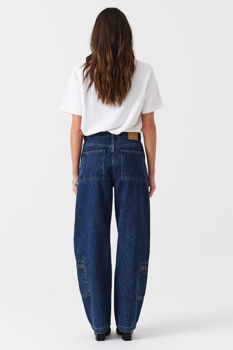 Woman wearing a white t-shirt and blue jeans with zip details on a white background photographed from the 
back