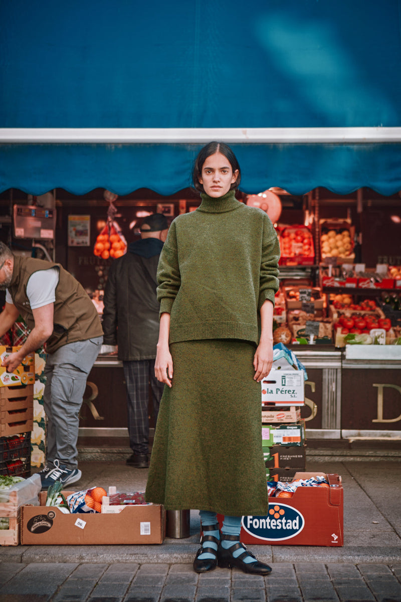 Person wearing a green L'ENVERS outfit standing in front of a market
