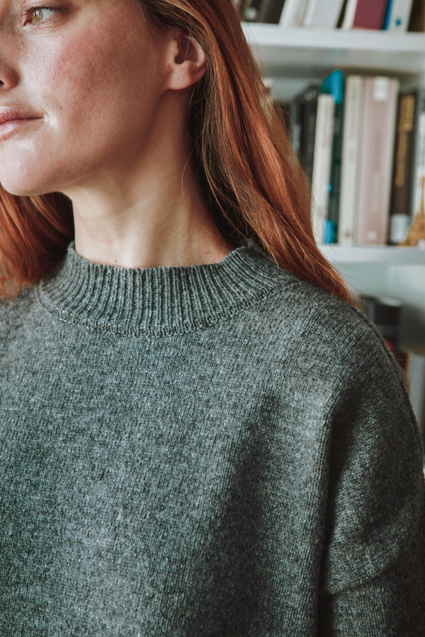Person wearing a grey dress with a blurred background of books on a shelf