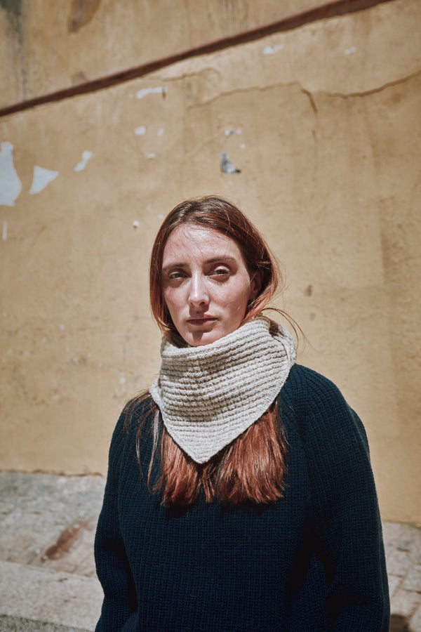 Woman wearing a textured beige scarf against a textured wall