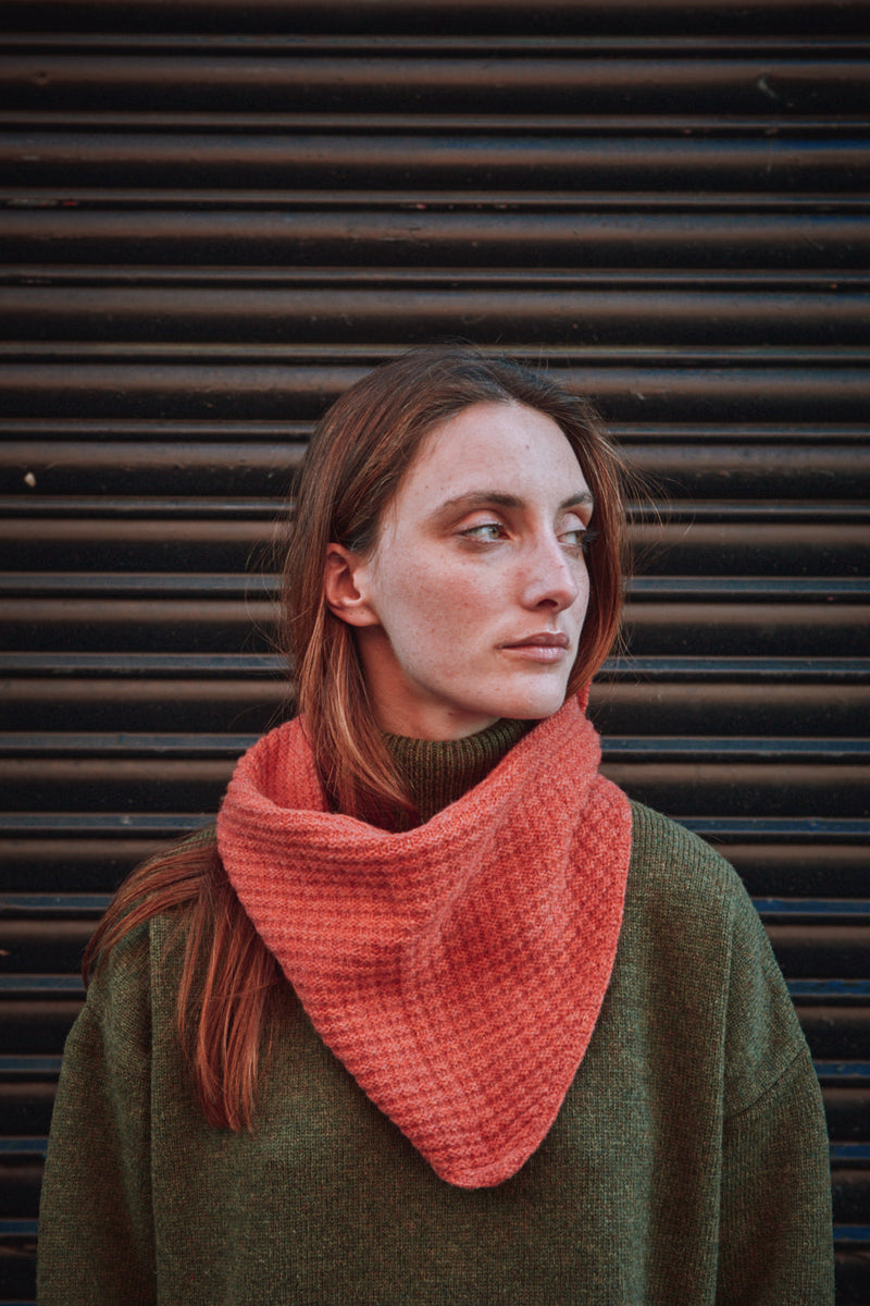 Woman wearing a coral scarf against a dark background