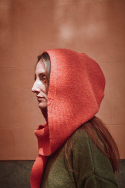 Person wearing a coral hooded garment against a brown background