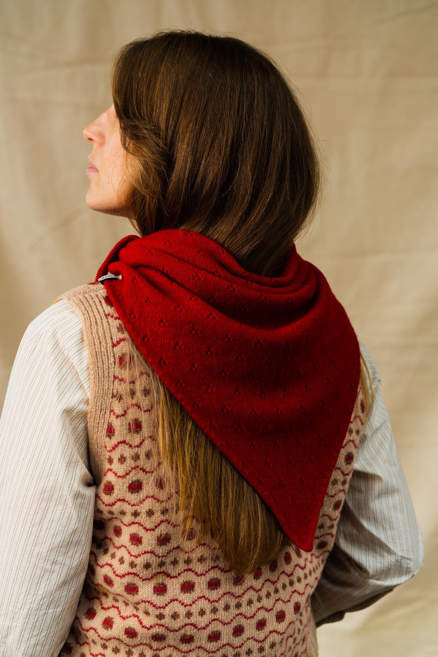 Person wearing a red knitted scarf over a patterned vest against a beige background