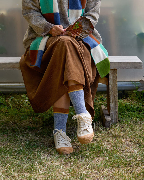 Model sitting on bench wearing blue marl organic cotton socks with brown cuff