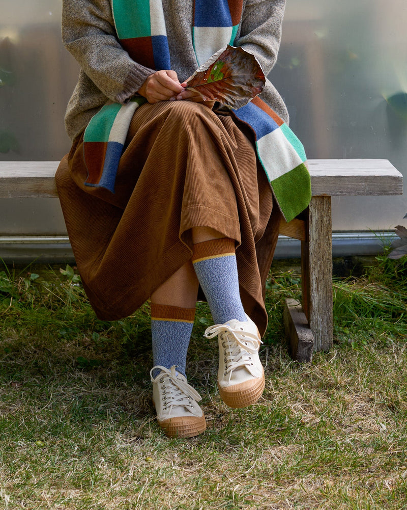 Model sitting on bench wearing blue marl organic cotton socks with brown cuff