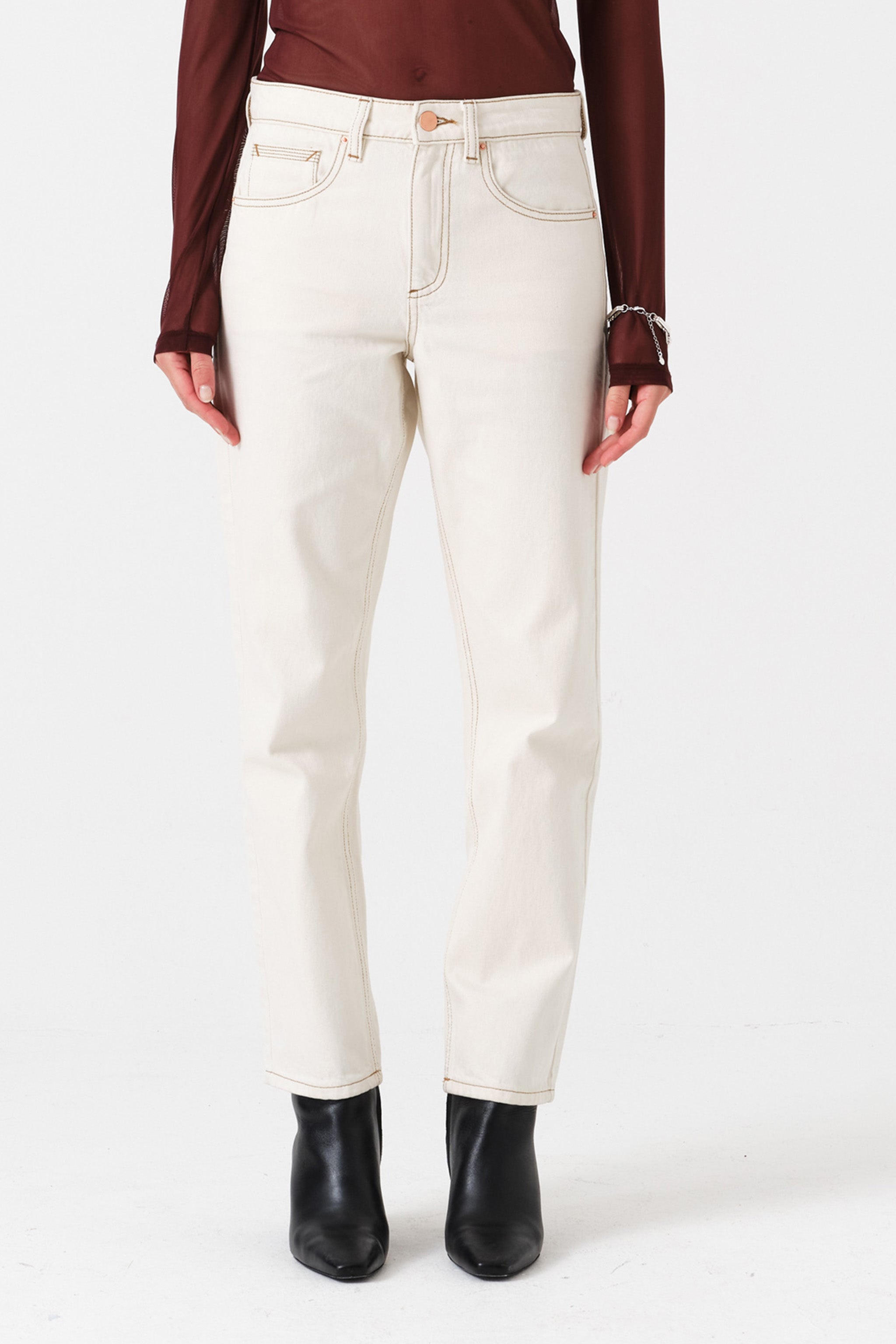 Woman wearing off white straight leg jeans and a brown shirt on a white background
