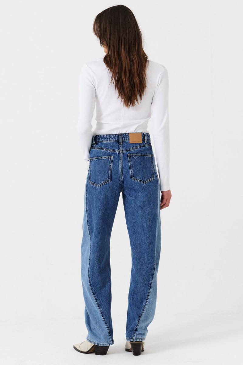 Woman wearing two toned blue barrel leg jeans and a white shirt on a white background