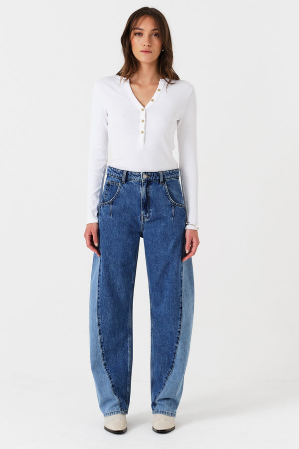 Woman wearing two toned blue barrel leg jeans and a white shirt on a white background