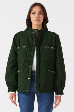 Woman wearing a quilted dark green jacket with white embroidered details and blue jeans on a white background