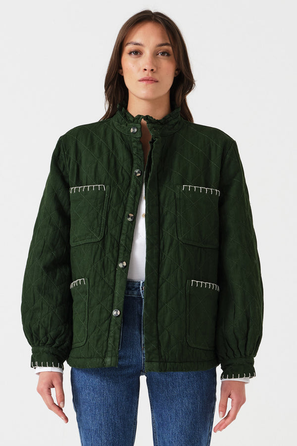 Woman wearing a quilted dark green jacket with white embroidered details and blue jeans on a white background