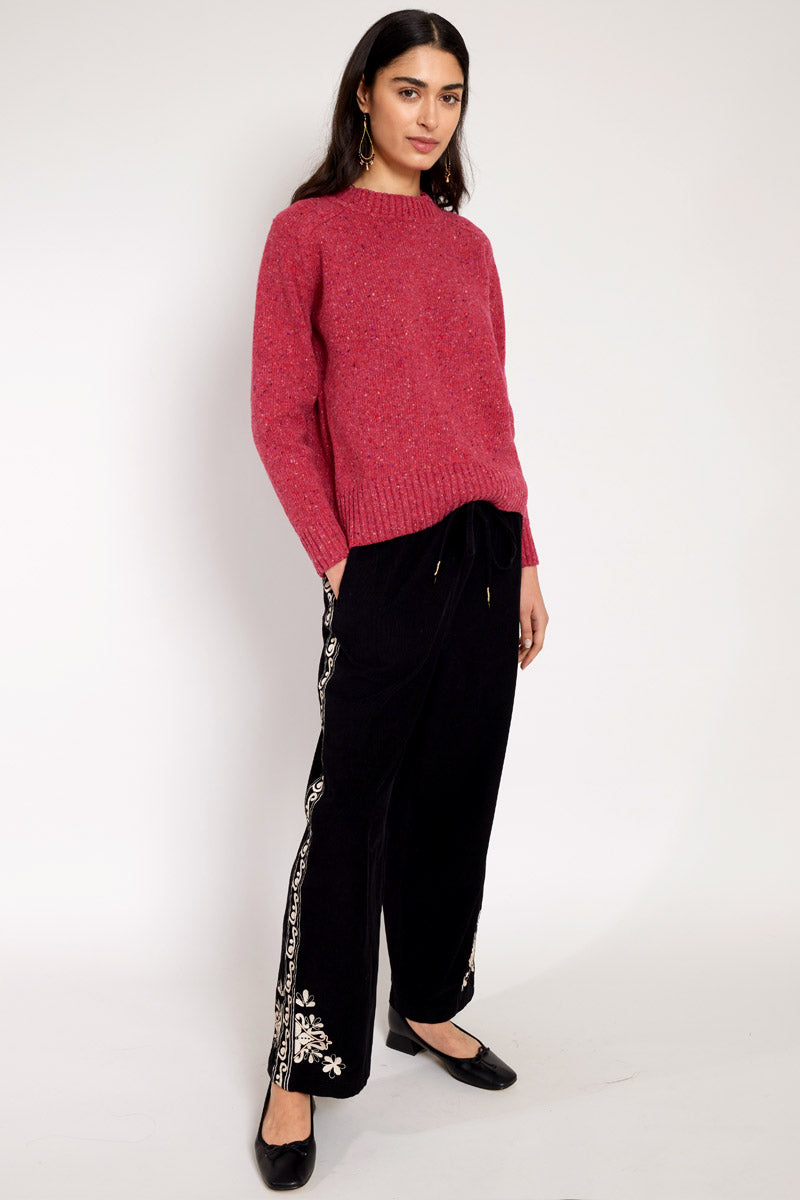 Side view of Model wearing East Eveline embroidered trousers, with pink Oubas knitted jumper
