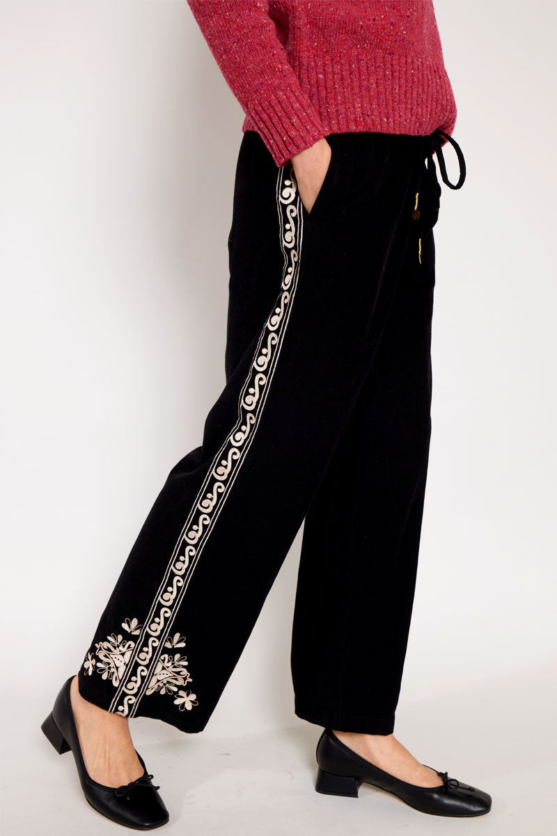 Side view of Models legs wearing East Eveline embroidered trousers, with pink Oubas knitted jumper
